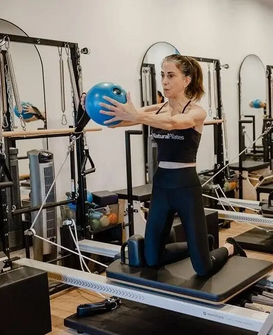 Lexy P doing Pilates on a reformer machine with a blue ball at Natural Pilates studio.
